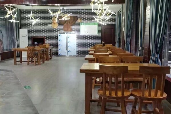 Un restaurante con mesas y sillas de madera, una pared de ladrillo y un candelabro colgante.