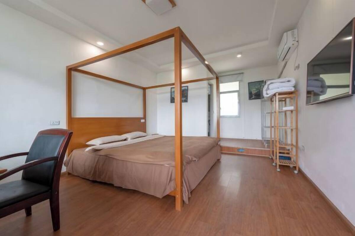 A room with a four-poster bed, a chair, a TV mounted on the wall, and a wooden ladder.