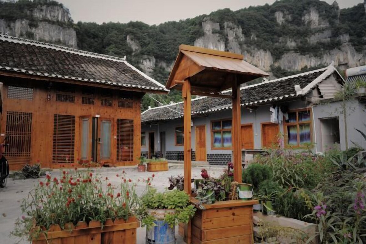 Traditional wooden buildings with tiled roofs, a wooden structure in the foreground, and a mountainous backdrop.