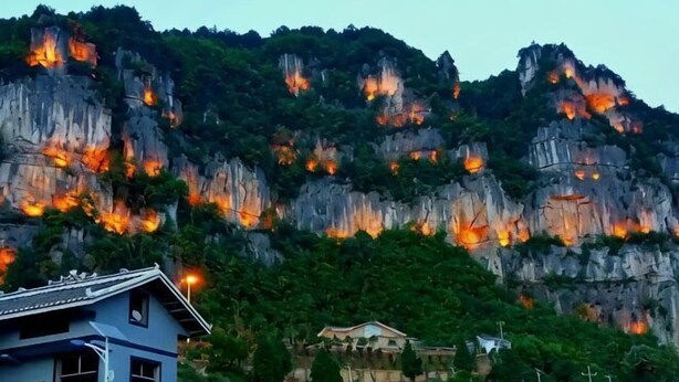 Una montaña con formaciones rocosas iluminadas y una casa en primer plano.