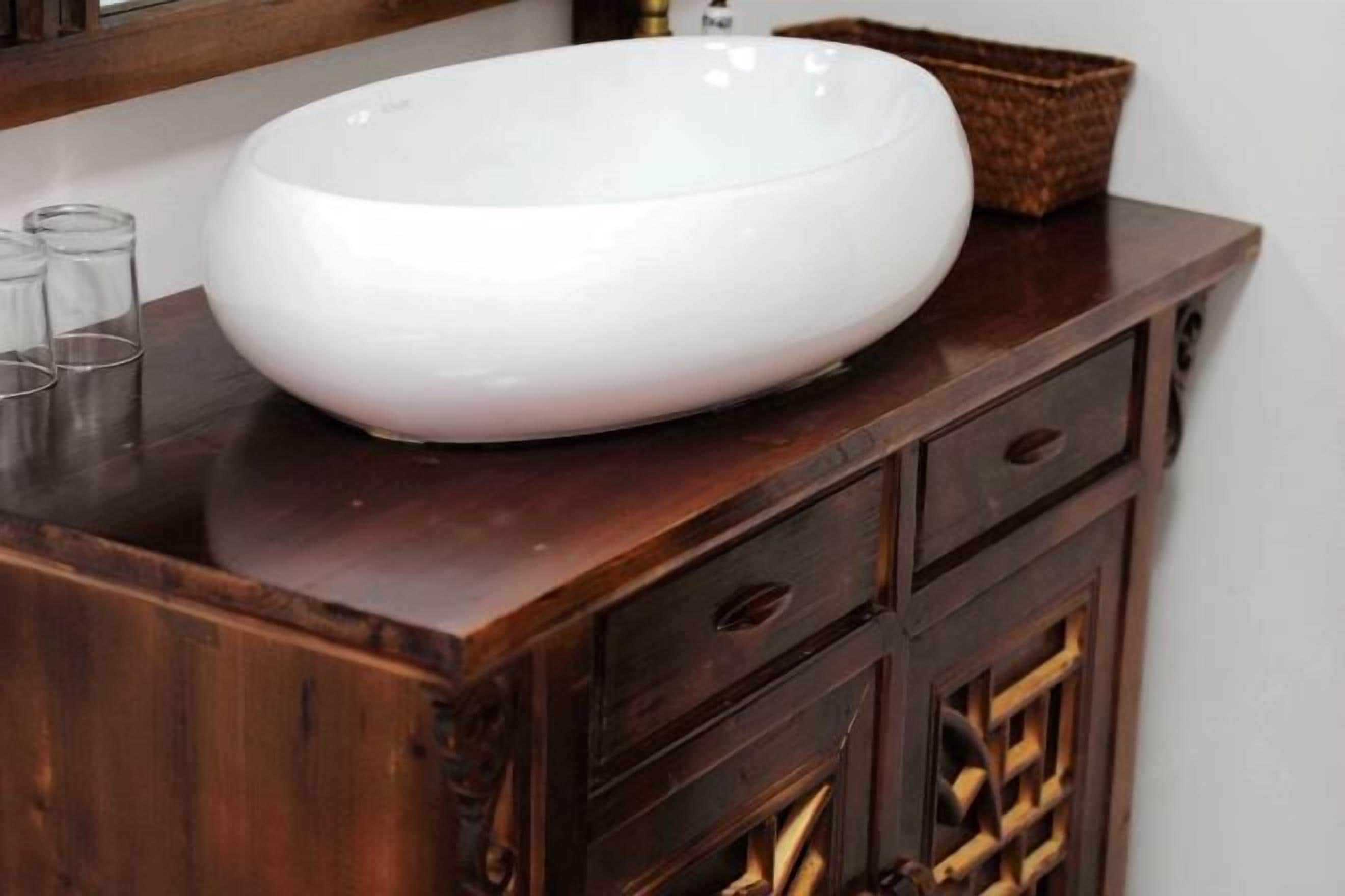 A white oval-shaped vessel on a wooden cabinet with drawers and a basket.