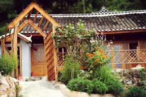 Ein traditionelles Holzhaus mit Ziegeldach, einer Holzveranda und einem Garten mit orangefarbenen Blumen.