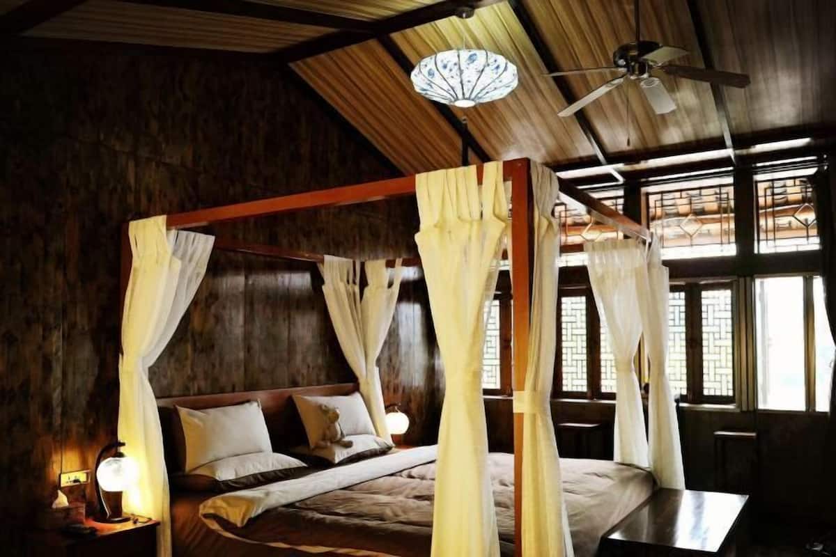A four-poster bed with white drapes, a ceiling fan, and a wooden ceiling.