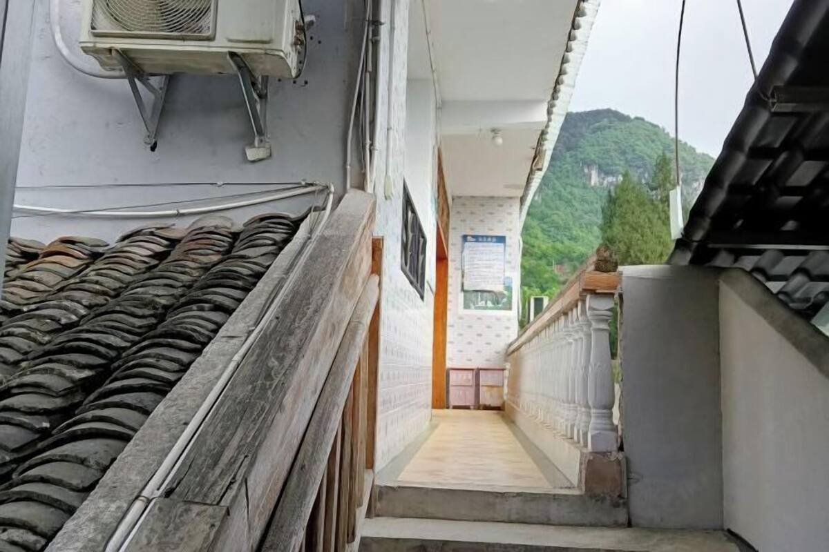 A narrow corridor with a tiled roof on one side and a balcony with a railing on the other. A small table and chairs are visible in the distance.
