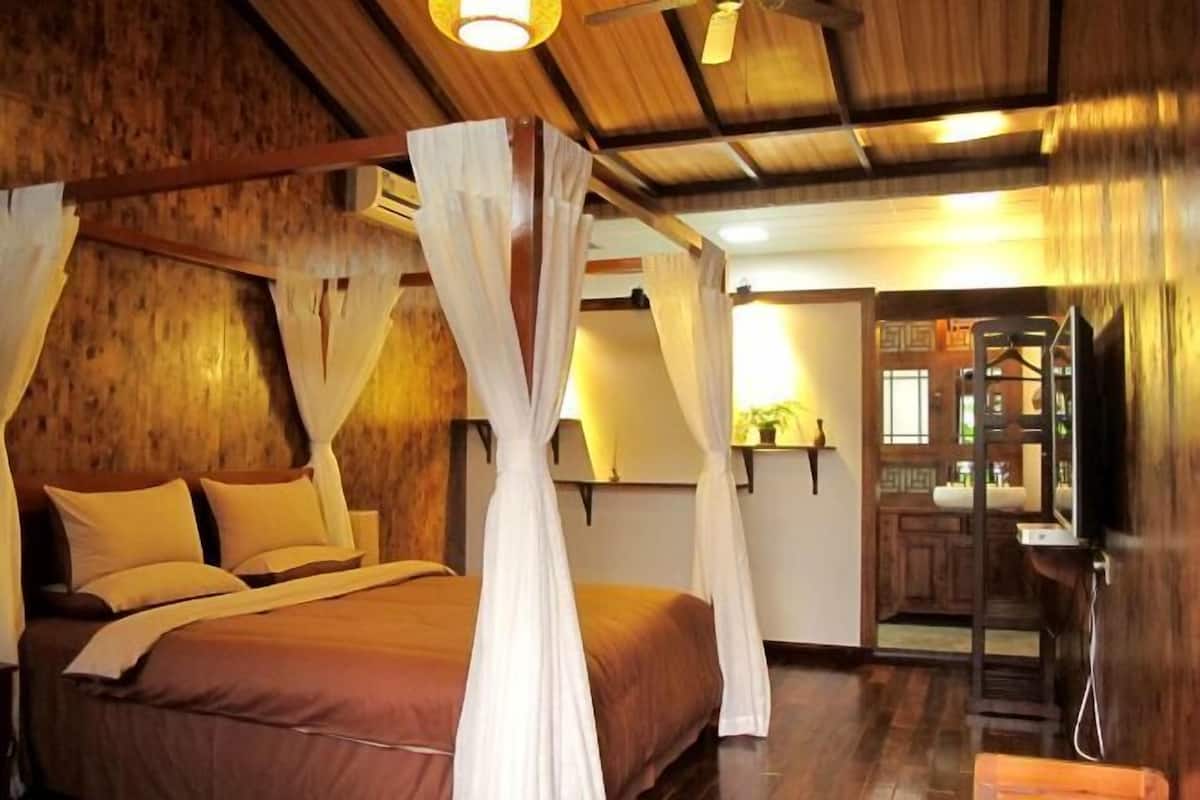 A room with a bed, wooden walls, a ceiling fan, and a small kitchenette.