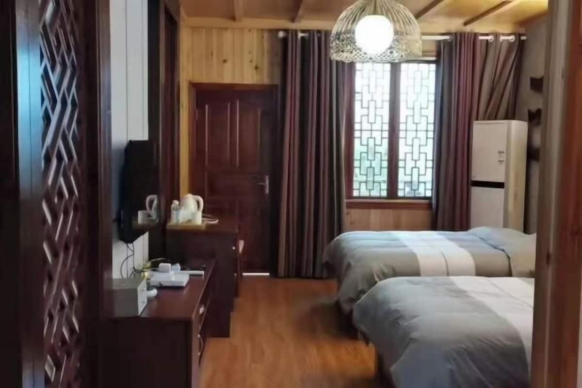 A room with wooden walls, a desk with a kettle, two beds, a wardrobe, and a window with curtains.