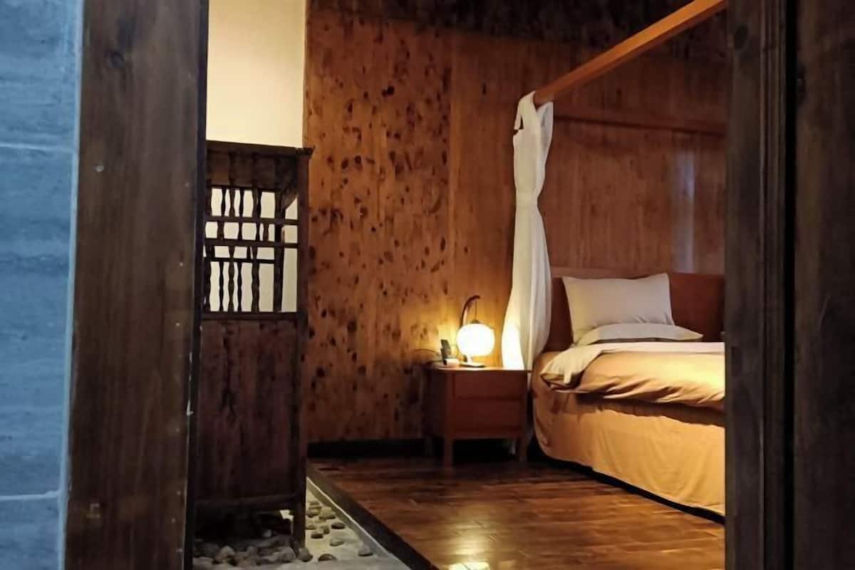 A wooden room with a bed, a nightstand with a lamp, and a wooden partition.