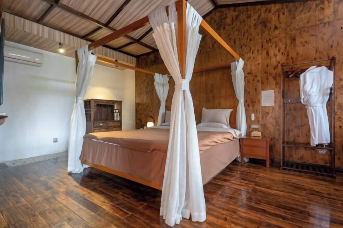 A four-poster canopy bed in a rustic room with wooden walls and floors.