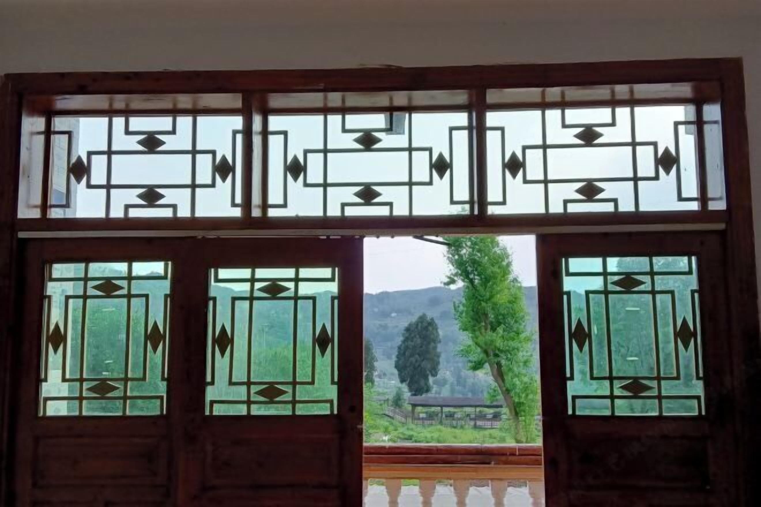 A wooden door with geometric glass patterns, leading to an outdoor area with a view of trees and hills.