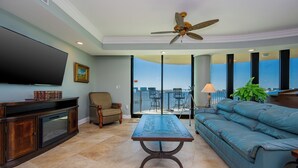 A living room with a flat-screen TV, a sofa, a coffee table, a chair, and a balcony with a view. - Poseidon House - Phoenix on the Bay 1333 (Orange Beach)