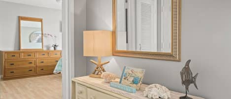 A room with a wooden dresser, a mirror with a gold frame, a lamp, and a card on the dresser.
