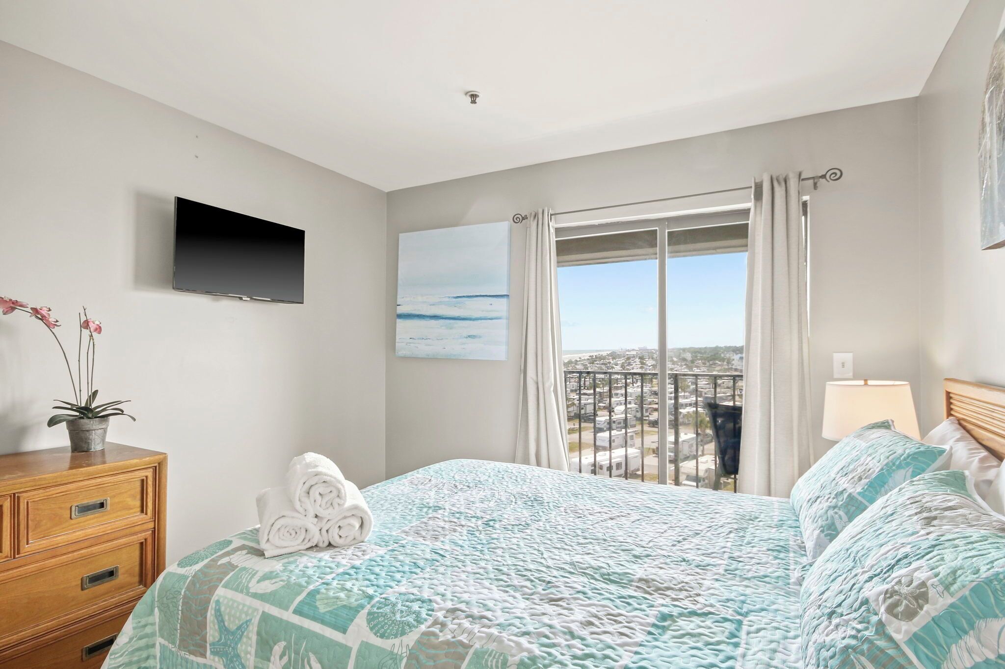 Ein Hotelzimmer mit Bett, Fernseher, Fenster mit Vorhängen, Pflanze und Blick auf die Stadt.