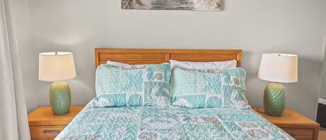 A bedroom with a wooden headboard, a patterned bedspread, two bedside lamps, and a wall-mounted picture of a pathway.