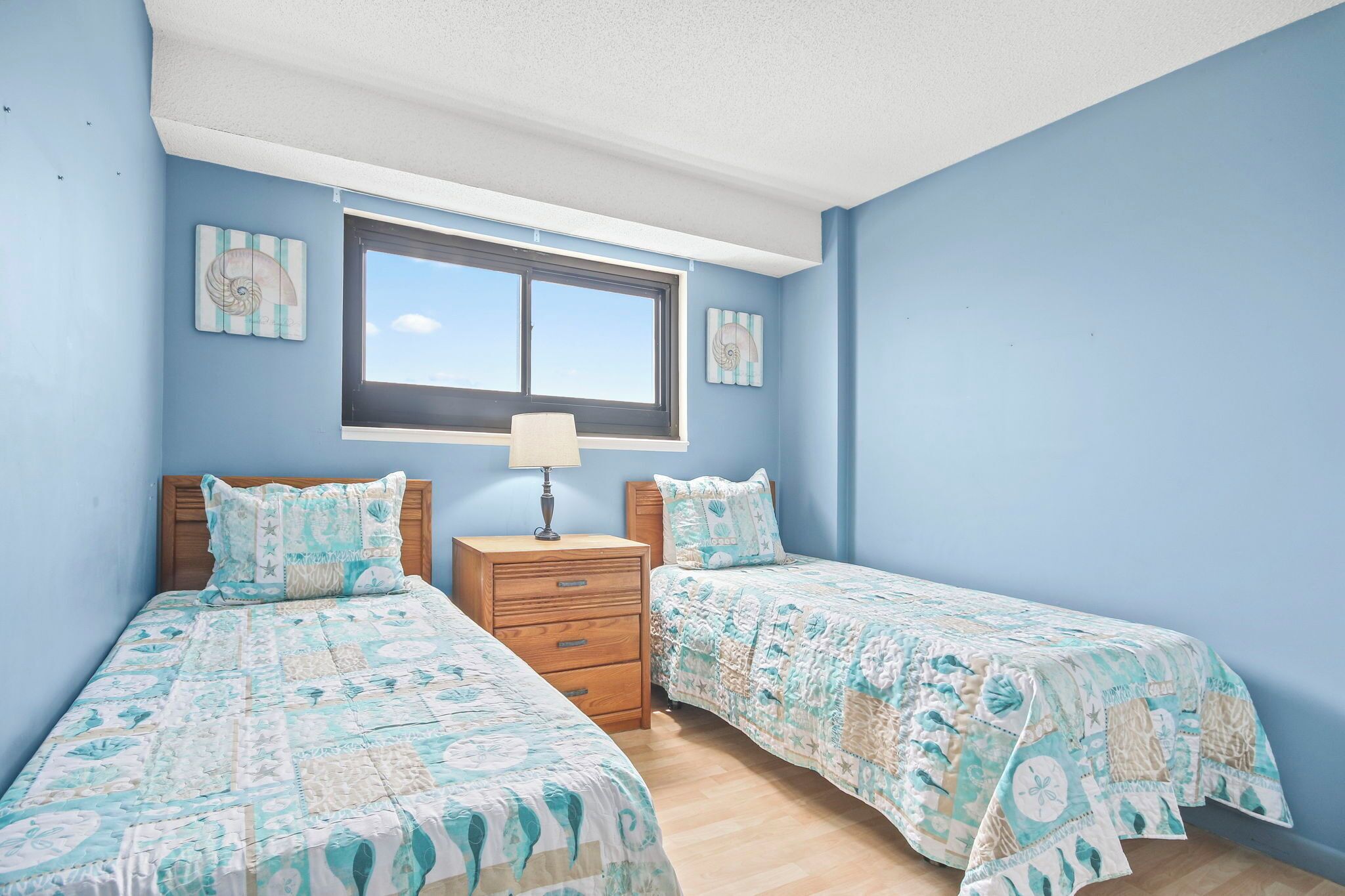 A bedroom with two beds, a nightstand, a window, and wall art.