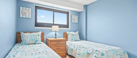 A bedroom with two beds, a nightstand, a window, and wall art.