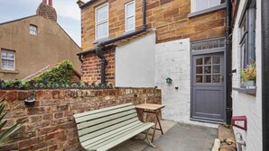 Une ruelle étroite avec un banc, une petite table et une porte dotée d’une fenêtre.