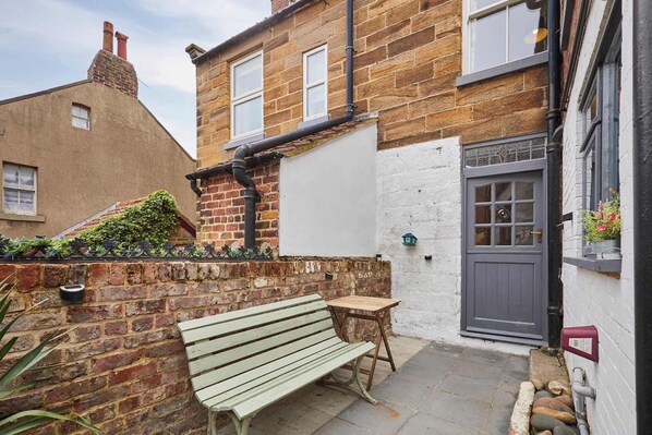A narrow alleyway with a bench, a small table, and a door with a window. - Host & Stay | Clarence Place (Whitby)