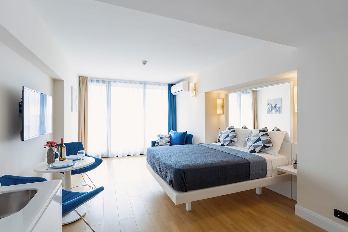A modern hotel room with a large bed, a desk with a chair, a TV, and a window with curtains.