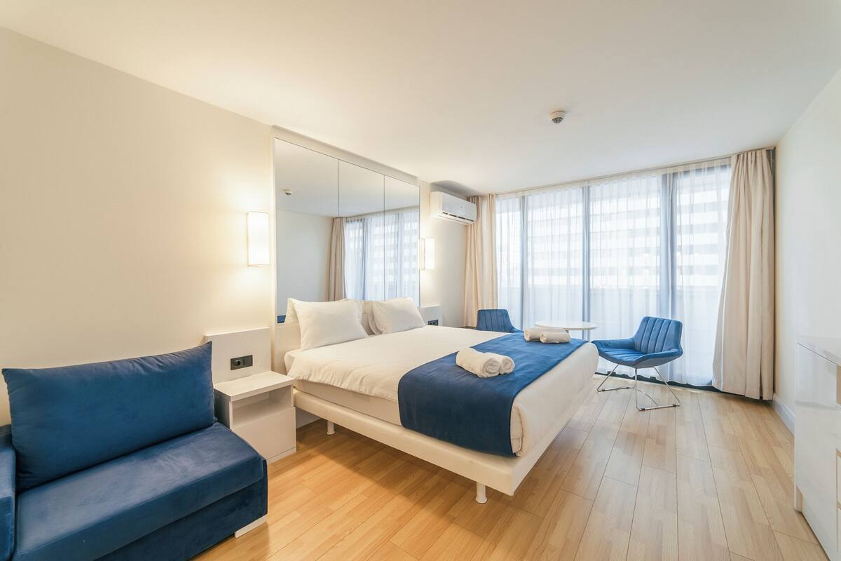 A hotel room with a bed, a blue sofa, a small table, and a chair.