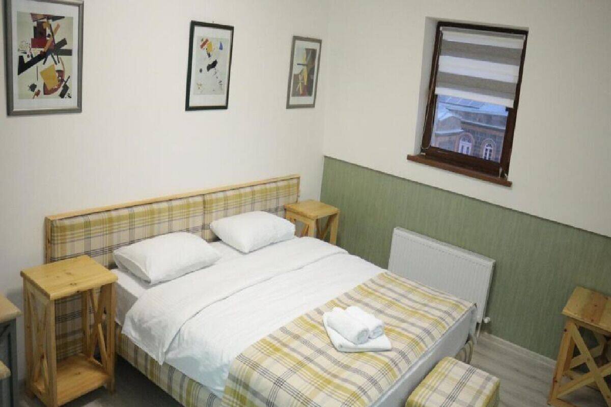 A bedroom with a bed, two bedside tables, a window, and three framed pictures on the wall.