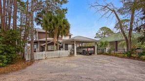 A two-story house with a covered porch and a gravel driveway. - Bayfront Dream: 3BR/3BA with Dock, Deck, Fireplace & Free Attraction Tickets! (Santa Rosa Beach)