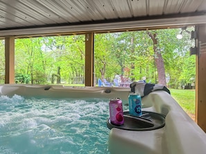 A hot tub with a view of a lush green landscape through large windows.
