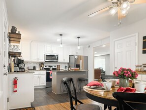 A modern kitchen with white cabinets, stainless steel appliances, and a dining area with a wooden table and chairs.