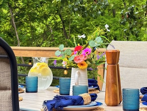A table set outdoors with a pitcher of lemonade, a vase of flowers, and blue glassware.