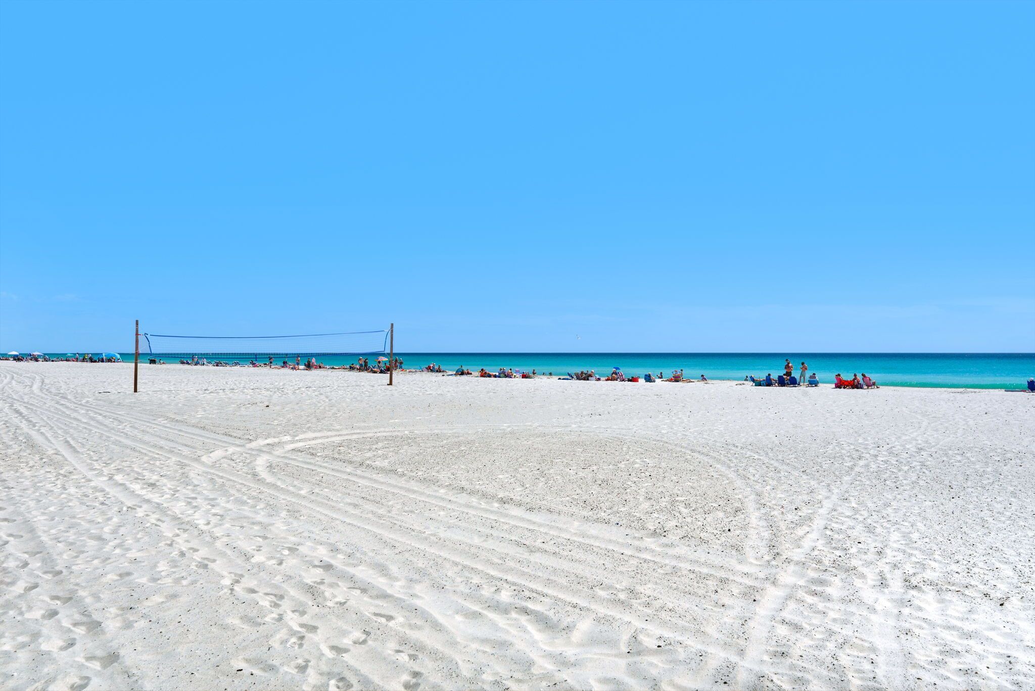 Una playa con una red de voleibol, cielo azul despejado y una orilla arenosa.
