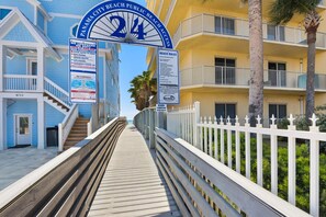 A wooden boardwalk leading to a beach area with a sign indicating no lifeguard on duty and beach rules.