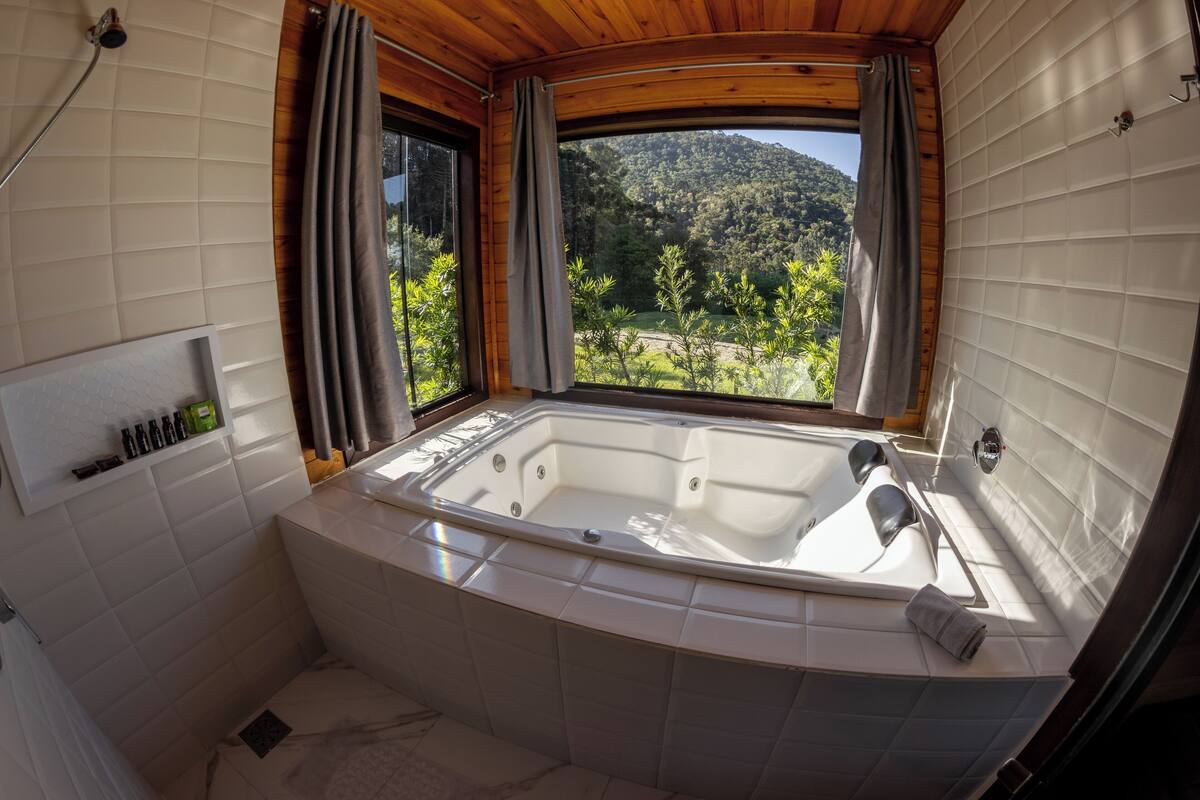 A bathroom with a large bathtub, wooden ceiling, and a window with curtains.