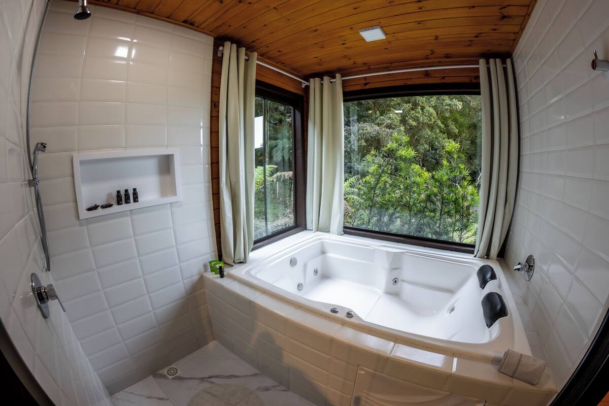 A modern bathroom with a large bathtub, a shower, and a window with curtains.