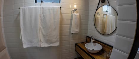 Un baño con paredes de azulejos blancos, un tocador de madera, un espejo redondo y dos toallas colgadas en ganchos.