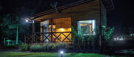A modern wooden cabin with a large open porch, a satellite dish, and a well-lit entrance.
