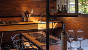 Interior de madera con cocina, mesa de comedor, sillas y vistas a zonas verdes.