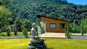 Un entorno exterior tranquilo con una estatua en un estanque, un edificio moderno y una montaña verde y exuberante al fondo.