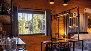 Acogedora habitación tipo cabaña con interior de madera, una cama con dosel, una mesa con sillas y un gran ventanal con vistas a árboles.