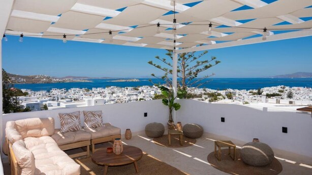 Terraza en la azotea con un área de estar exterior blanca, una planta en maceta y vistas a un pueblo costero.