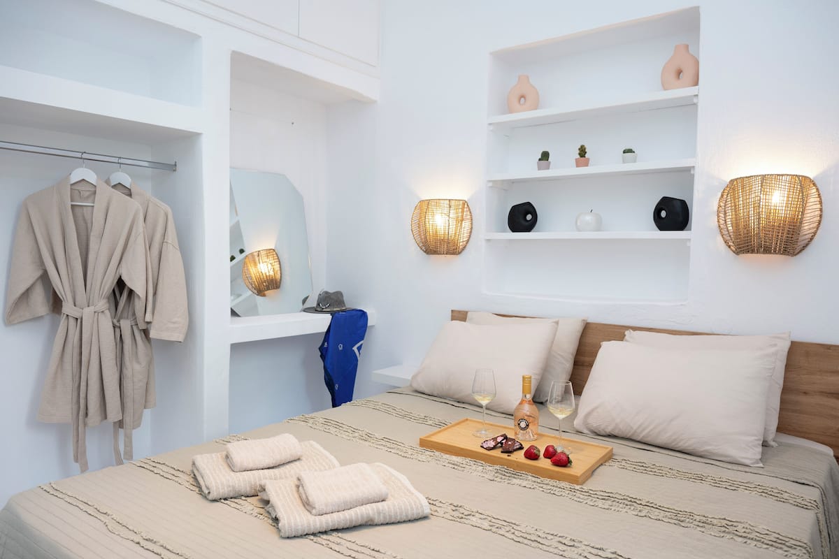 A hotel room with a bed, a robe rack, a shelf with decorative items, and wall-mounted sconces.