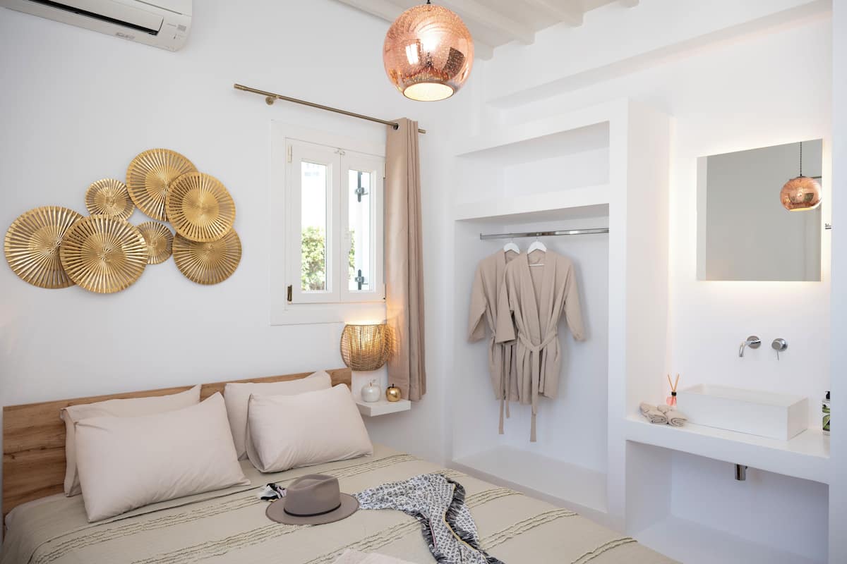 A bedroom with a bed, bedside table, lamp, and a view of a bathroom with a sink and mirror.