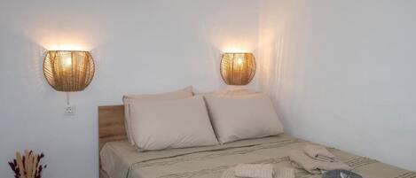 Una cama con cabecera, dos lámparas de pared, un jarrón con flores secas y un sombrero sobre la cama.