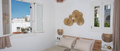 Un dormitorio con cama, mesitas de noche, una lámpara colgante y vistas a edificios.