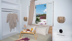 Un dormitorio con cama, una mesita de noche con desayuno, una ventana con vistas y una bata colgada en un perchero.