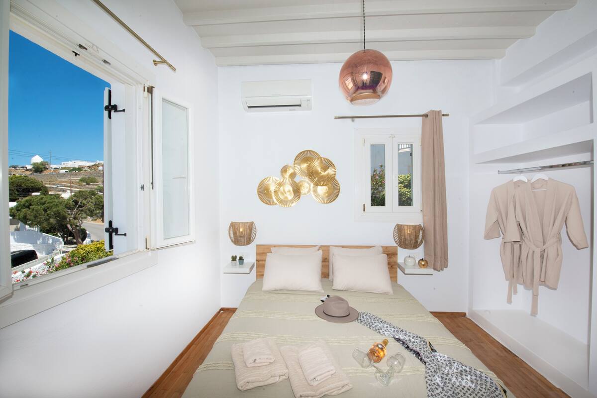 A bedroom with a large bed, a view of the outside, a hanging light, and a robe on the wall.