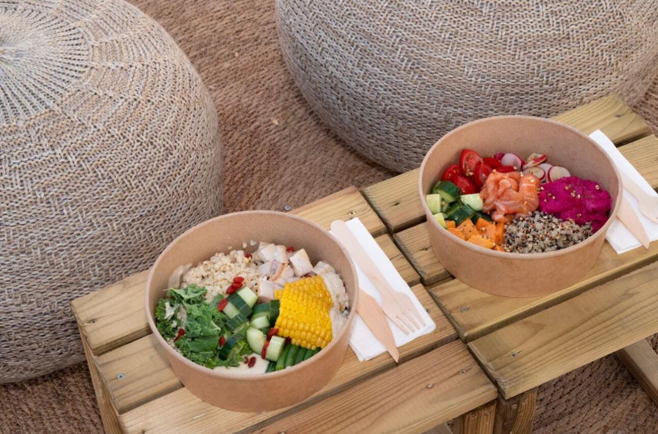 Two bowls of food on a wooden table with a woven cushion in the background.