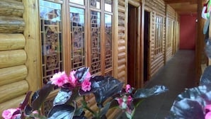 Interior de una cabaña de madera con paredes de madera, un pasillo y una puerta que da a otra habitación.