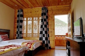 Een kamer met houten lambrisering, een bed, gordijnen, een televisie en uitzicht op een berg.