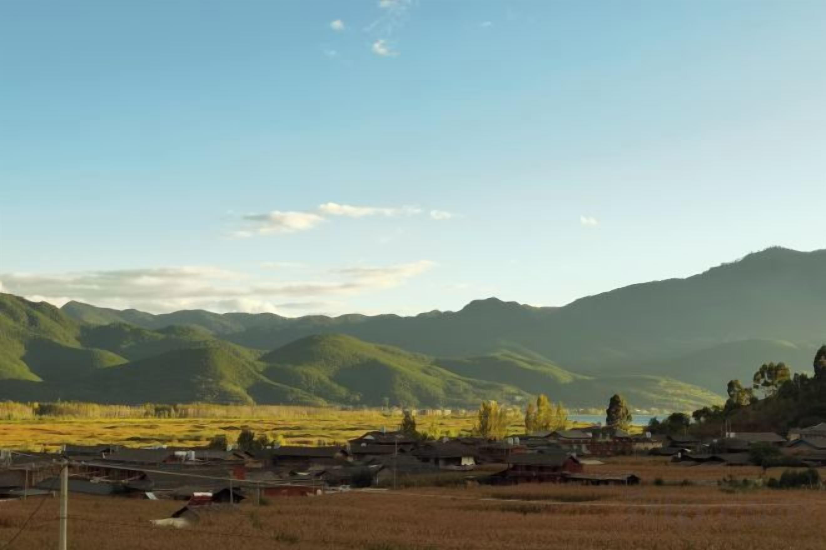 Un paysage rural avec des montagnes, un ciel dégagé et des bâtiments traditionnels.