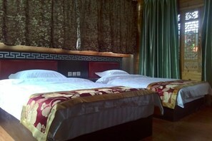 A hotel room with two beds, a wooden headboard with a geometric pattern, and a view through a window with green curtains. - Abu Ayao Inn (Yanyuan)