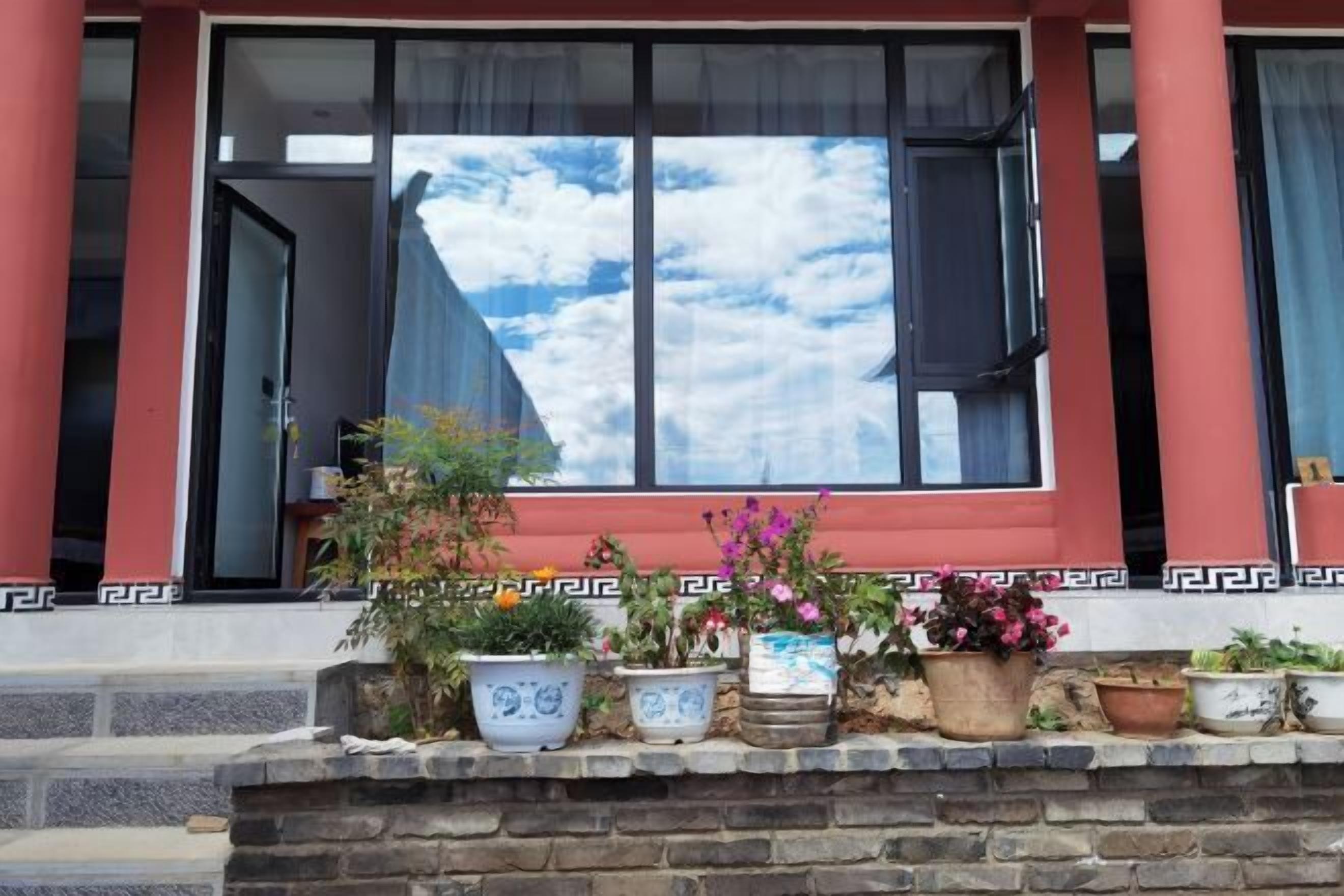 Un edificio con fachada roja, ventanas amplias de marcos negros y un balcón con plantas en macetas.